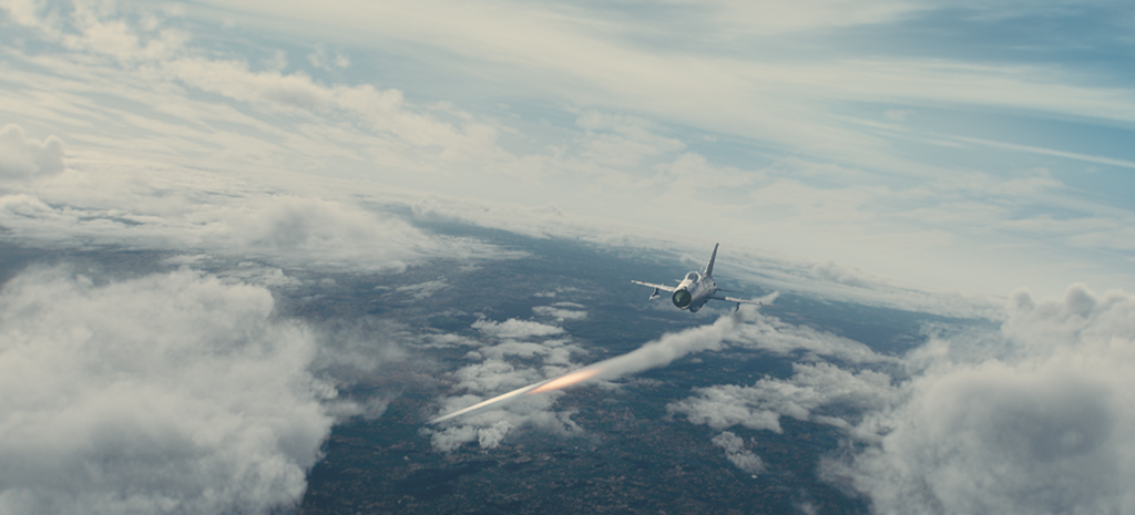 A CG MiG-21 fighter fires heat-seeking missiles, causing a mid-air explosion that alters Soyuz’s re-entry trajectory.